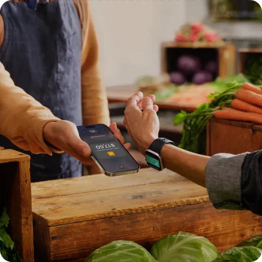Un cliente paga con su Apple Watch en un puesto de verduras usando Tap to Pay en iPhone.